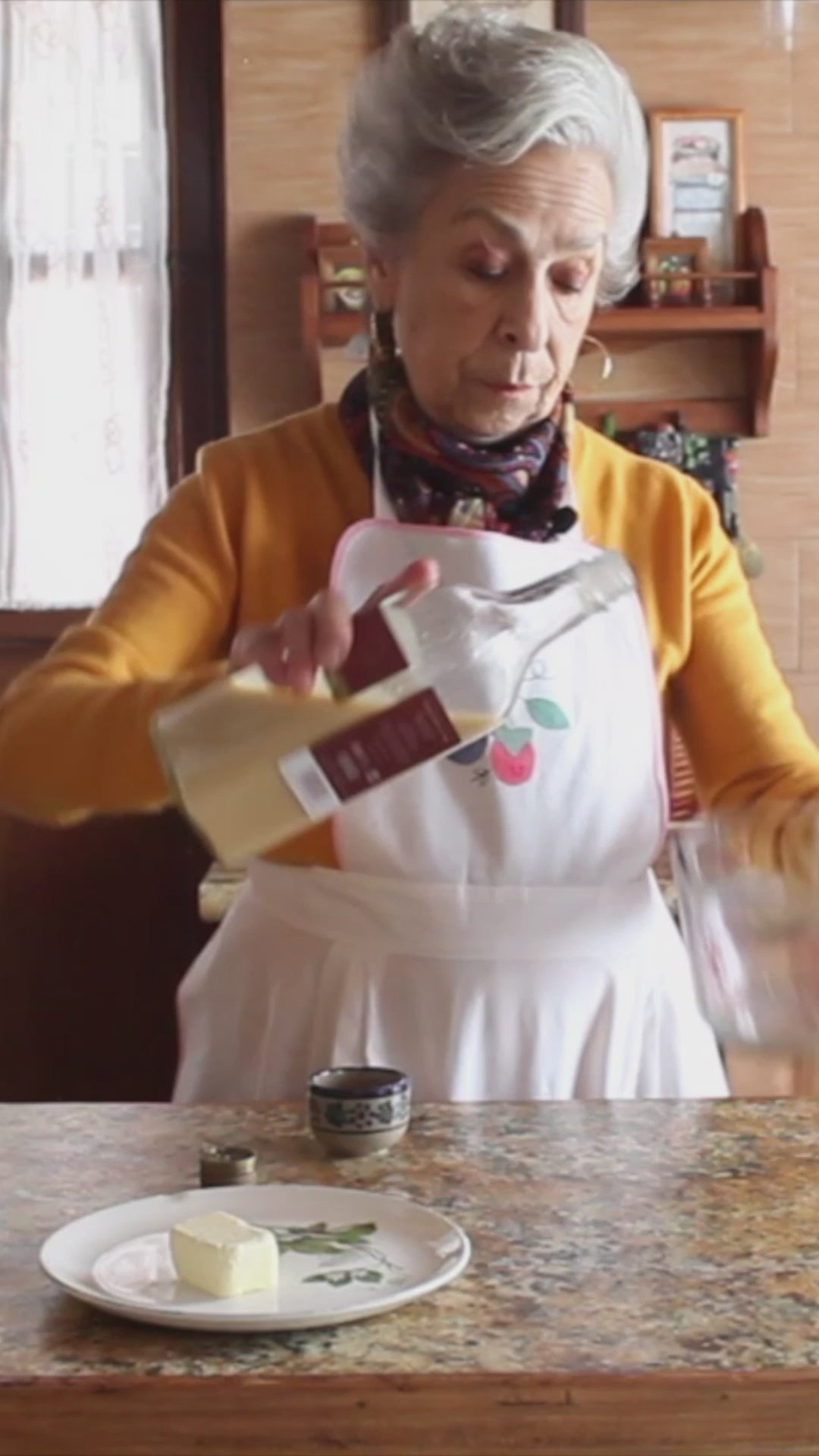 Video de una mujer mayor contando la historia tradicional y el origen artesanal del Rompope Carmelita, grabada en una ventana con fondo natural.